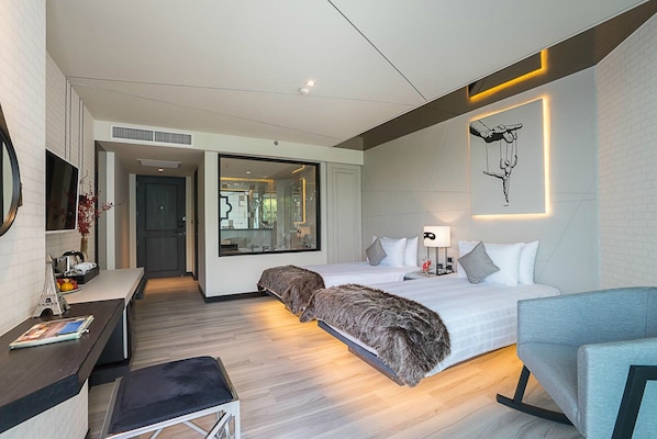 A modern hotel room with a large bed, a desk, and a chair. There is a large window and a wall-mounted artwork.