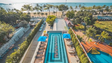 Relax by the infinity pool overlooking the ocean and beach, surrounded by lush greenery and palm trees.