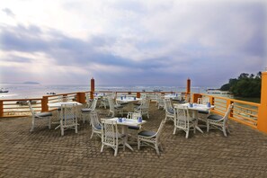 An outdoor dining area with white wicker chairs and tables, overlooking a body of water with boats and a distant island. - Fisherman's Bay (Weligama)