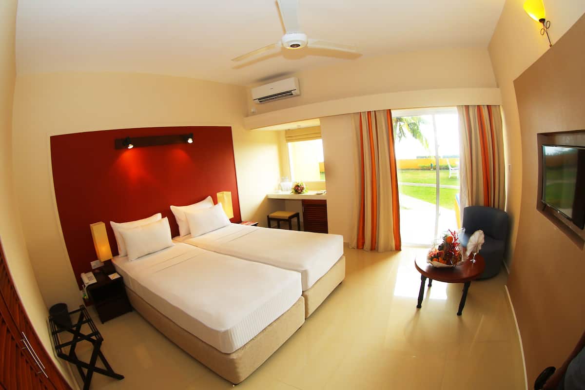 A hotel room with two beds, a desk, a chair, a TV, and a view of the outdoors.