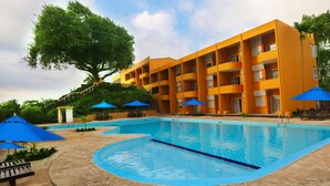Un hotel con piscina, sombrillas azules y un gran árbol.