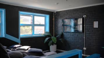 A room with a bed, a potted plant, a window, and a wall-mounted TV.
