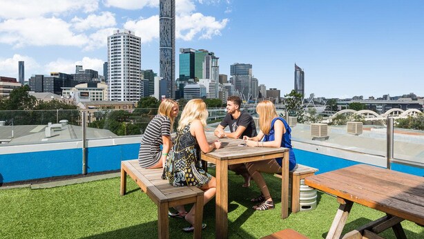 A rooftop terrace with a city skyline view, wooden furniture, and a pool. - Summer House Brisbane - Hostel (Brisbane)
