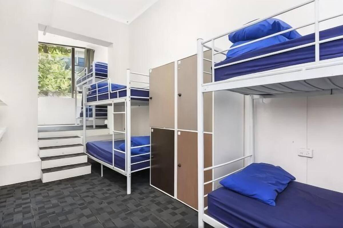 A dormitory room with bunk beds, a window with a view, and a staircase.