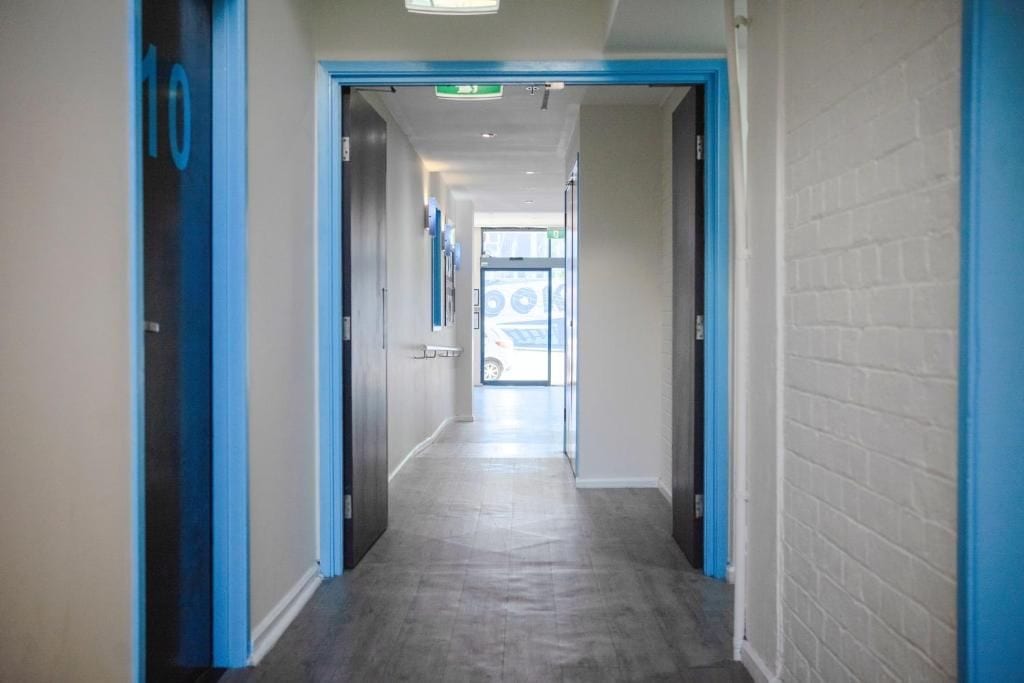 A hallway with doors marked with numbers, leading to a bright room with a car visible through the glass door.