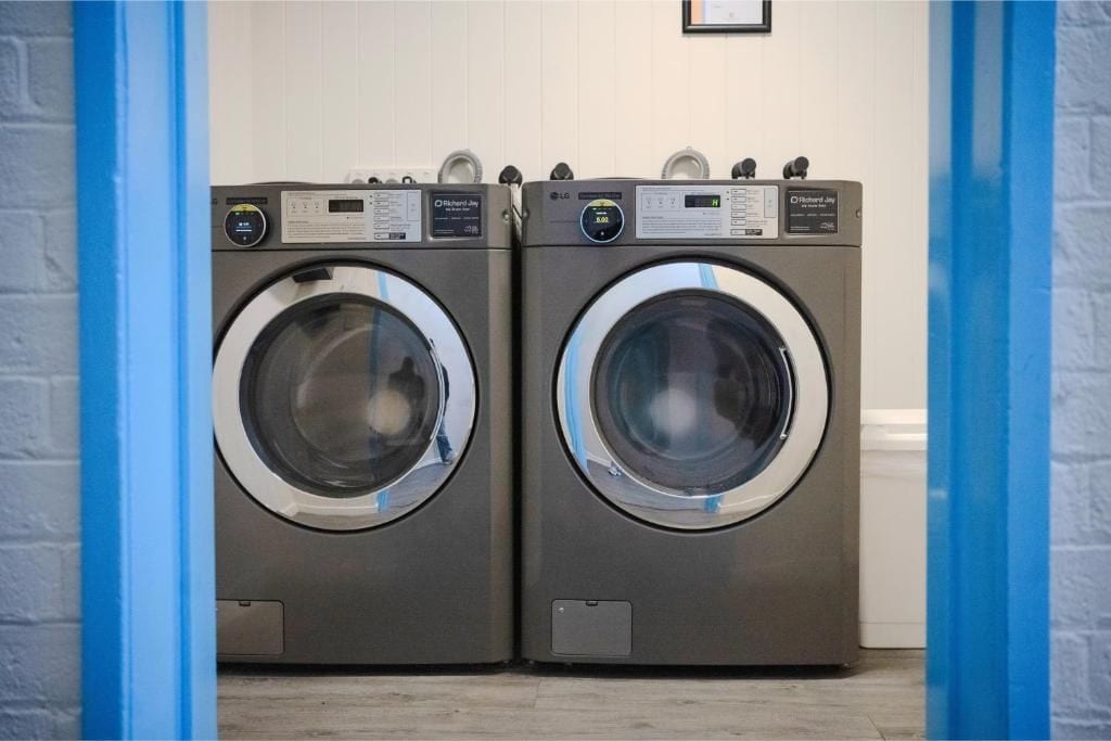 Two front-loading washing machines in a laundry room with a blue door frame.