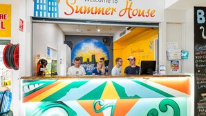 A colorful reception desk at Summer House with a cityscape mural and a chalkboard listing events. - Summer House Brisbane - Hostel (Brisbane)