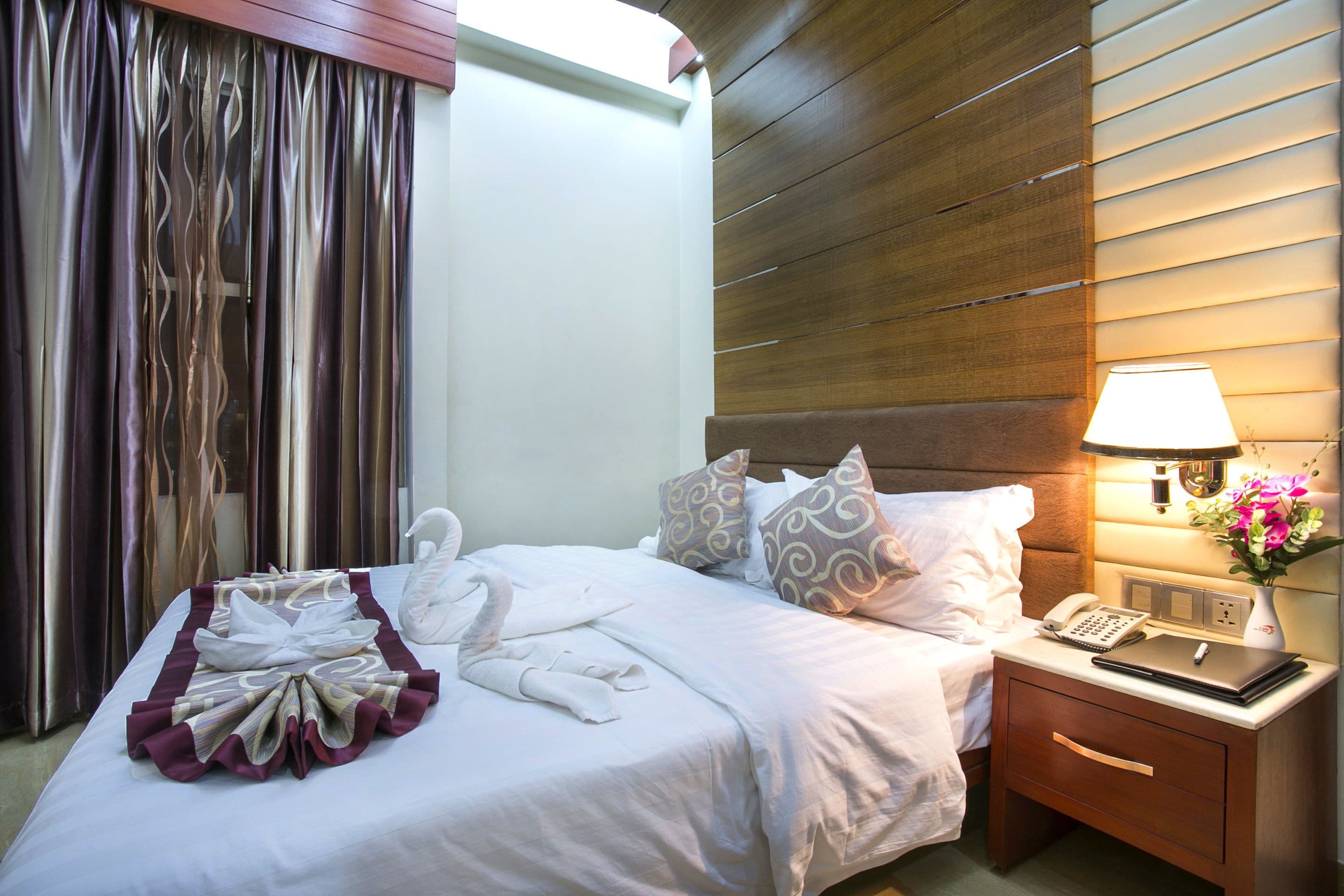 Quarto de hotel com cama bem arrumada, abajur, telefone e mesa de cabeceira com um vaso de flores.