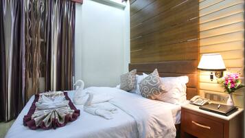 Quarto de hotel com cama bem arrumada, abajur, telefone e mesa de cabeceira com um vaso de flores.