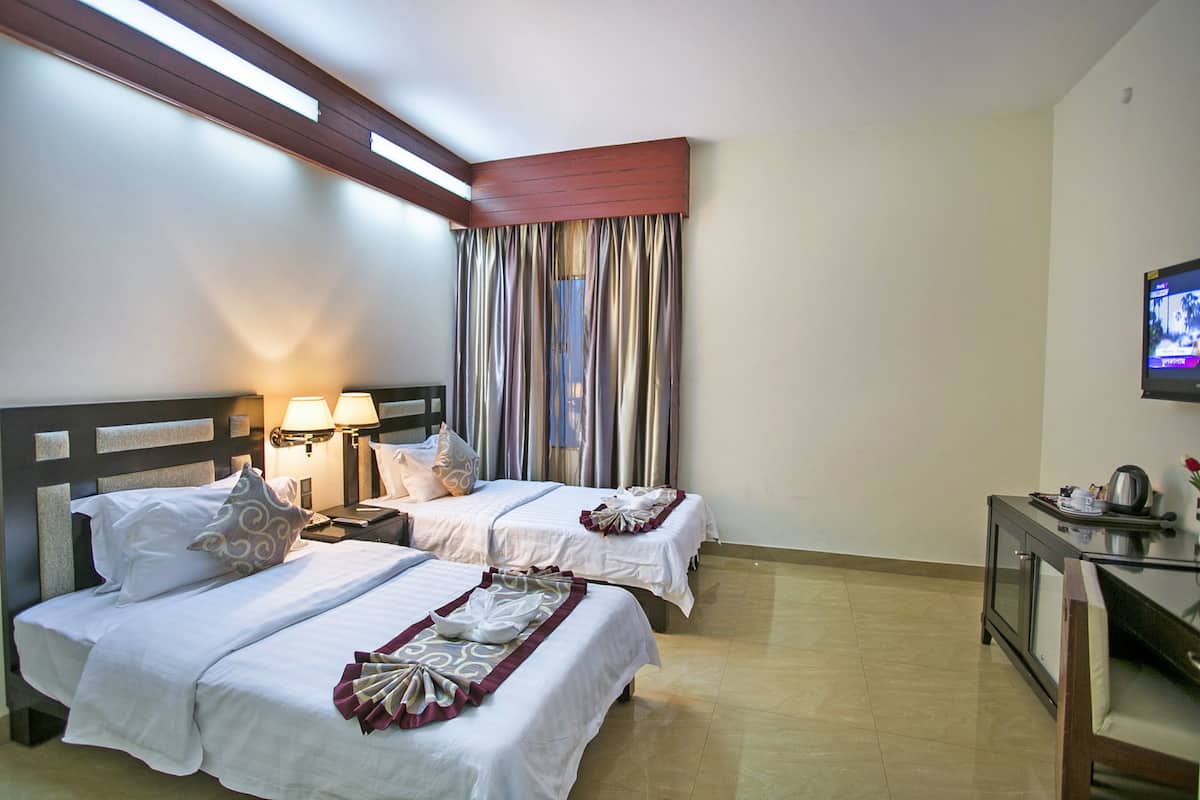 A hotel room with two beds, a TV, a desk, and a window with curtains.