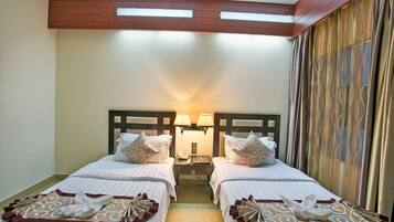 A hotel room with two beds, a nightstand with lamps, and a large window with curtains.
