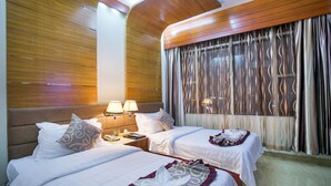 Ein Hotelzimmer mit zwei Betten, Holzwandverkleidung, einem großen Fenster mit Vorhängen und einem Nachttisch mit Lampe.