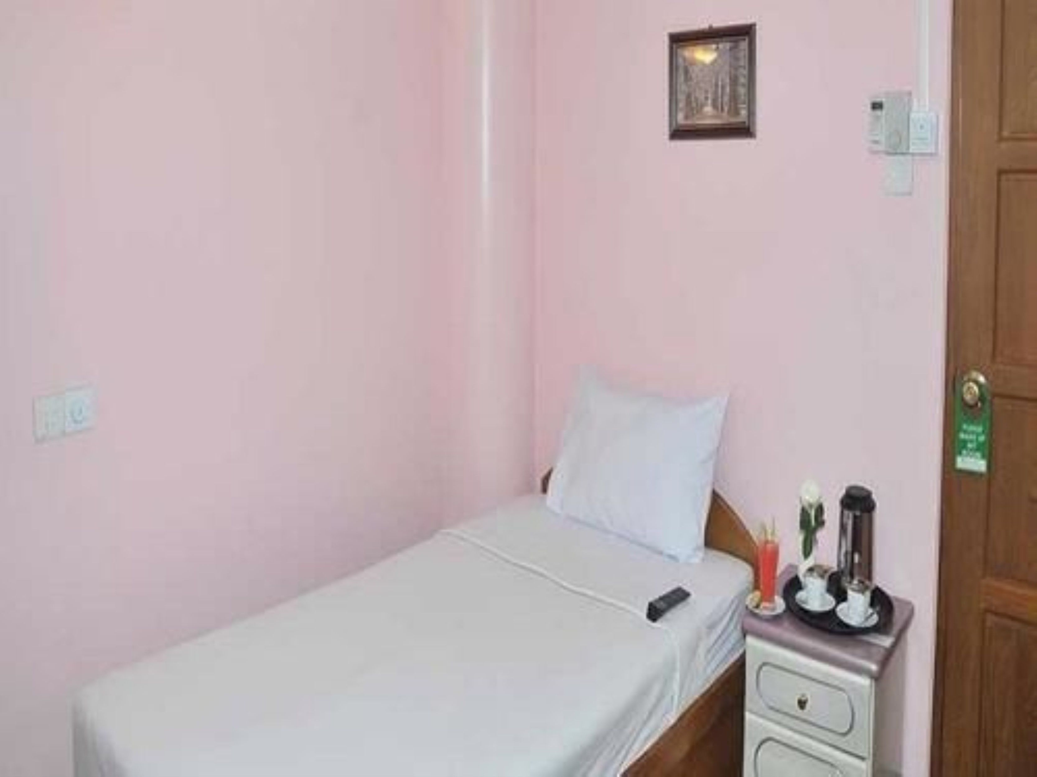 A small, single-bed room with a wooden headboard, a bedside table with a lamp, and a small picture frame on the wall.