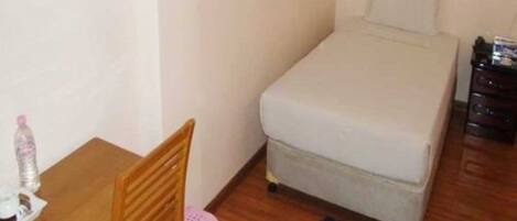 Una habitación pequeña y sencilla con una cama, una mesa de madera con una silla y un taburete.