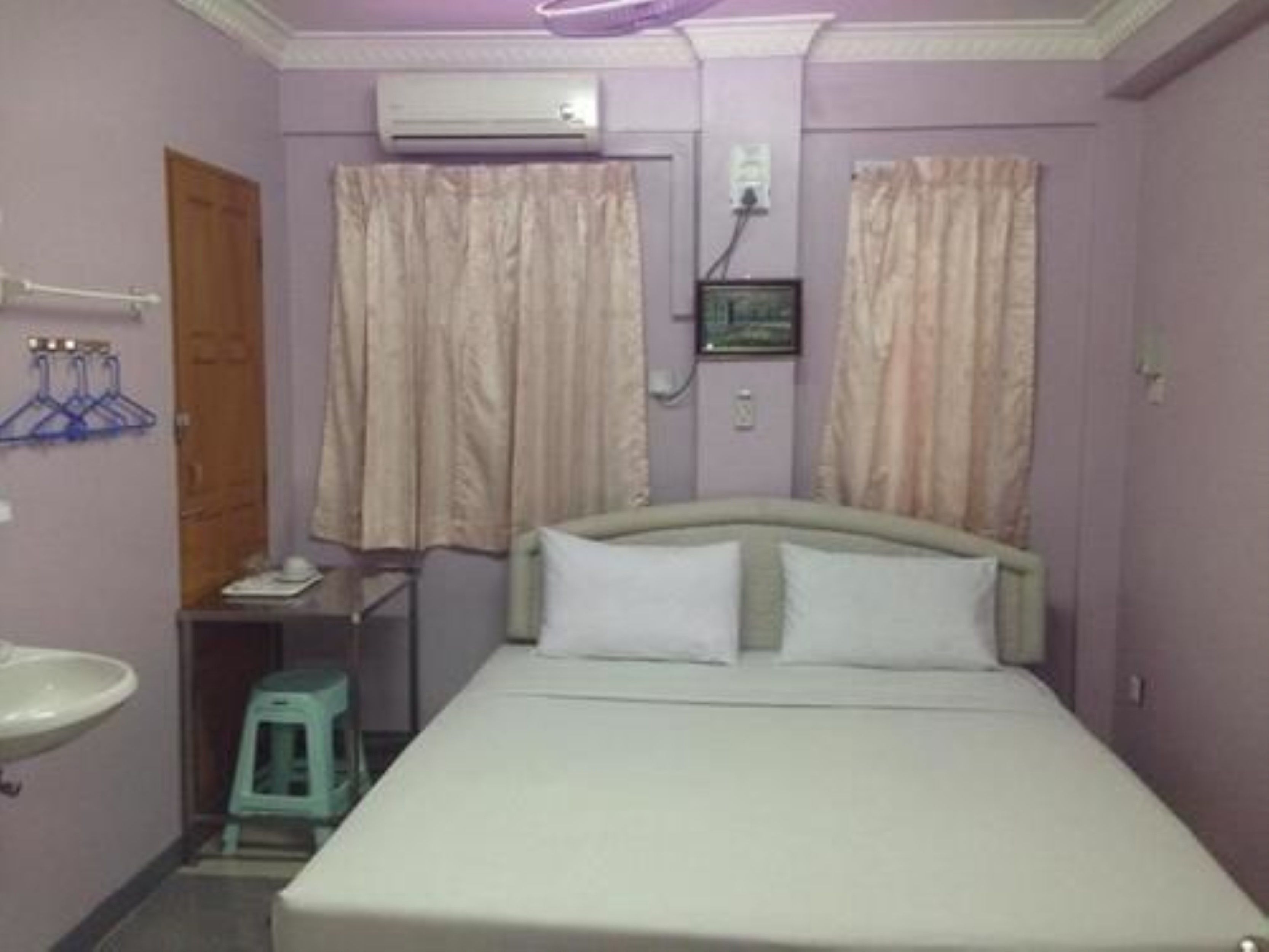 Un dormitorio con cama, mesita de noche, espejo, lavamanos y cortinas.