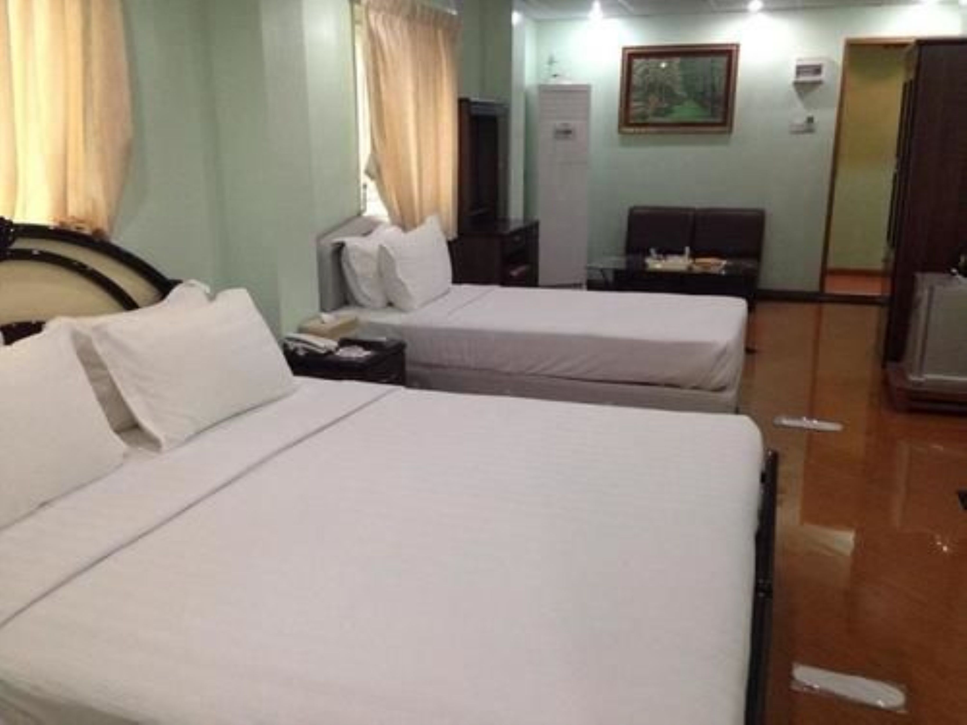 A hotel room with two single beds, a desk with a chair, a wardrobe, and a painting on the wall.