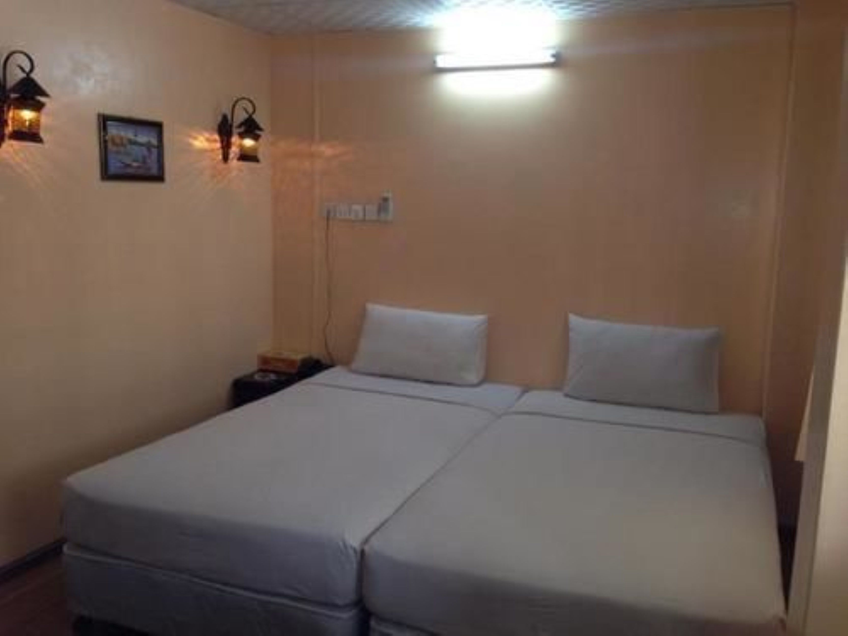 Habitación individual con una cama de madera, cabecera de madera, dos luces fijadas a la pared y una mesita de noche pequeña.