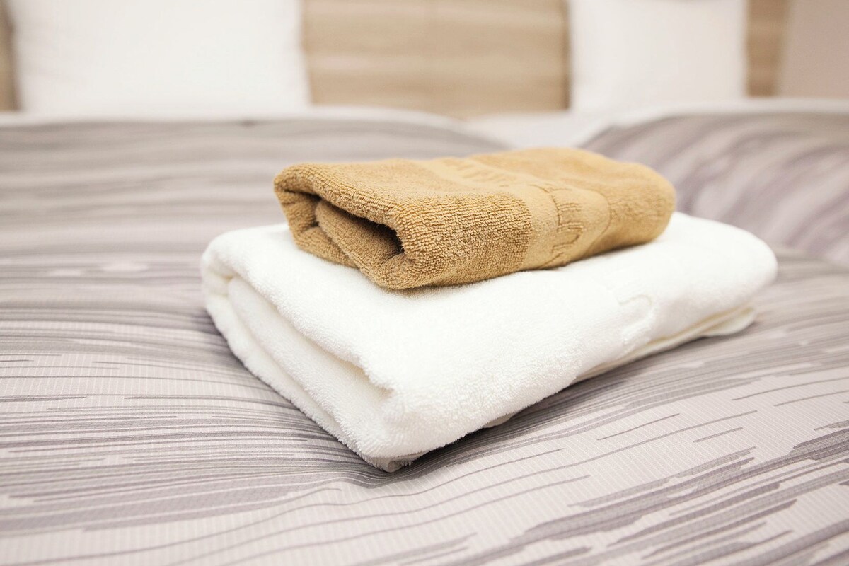 A neatly made bed with a folded beige towel and a folded white towel.