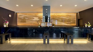 Un área de recepción con un mostrador de mármol negro, dos bancos de madera, un reloj y un separador decorativo con motivos de paisaje.