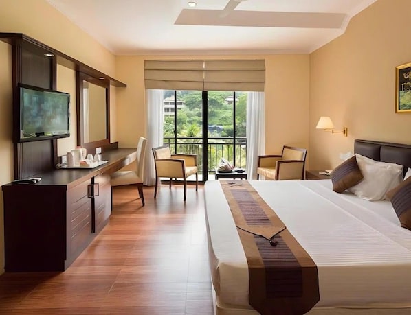 Habitación de hotel con cama, escritorio, silla, televisor y balcón con vistas.