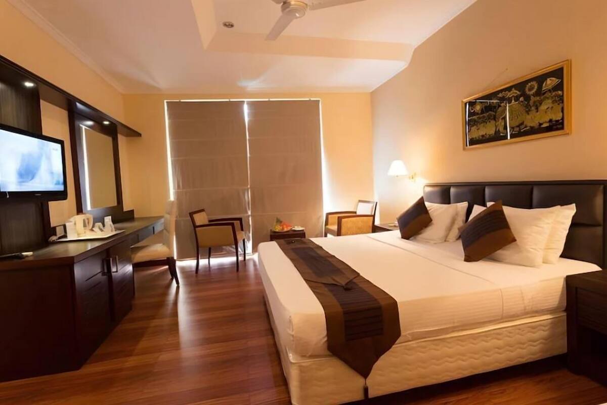 Ein Hotelzimmer mit Bett, Schreibtisch, Stuhl, Fernseher und einem Bild an der Wand.