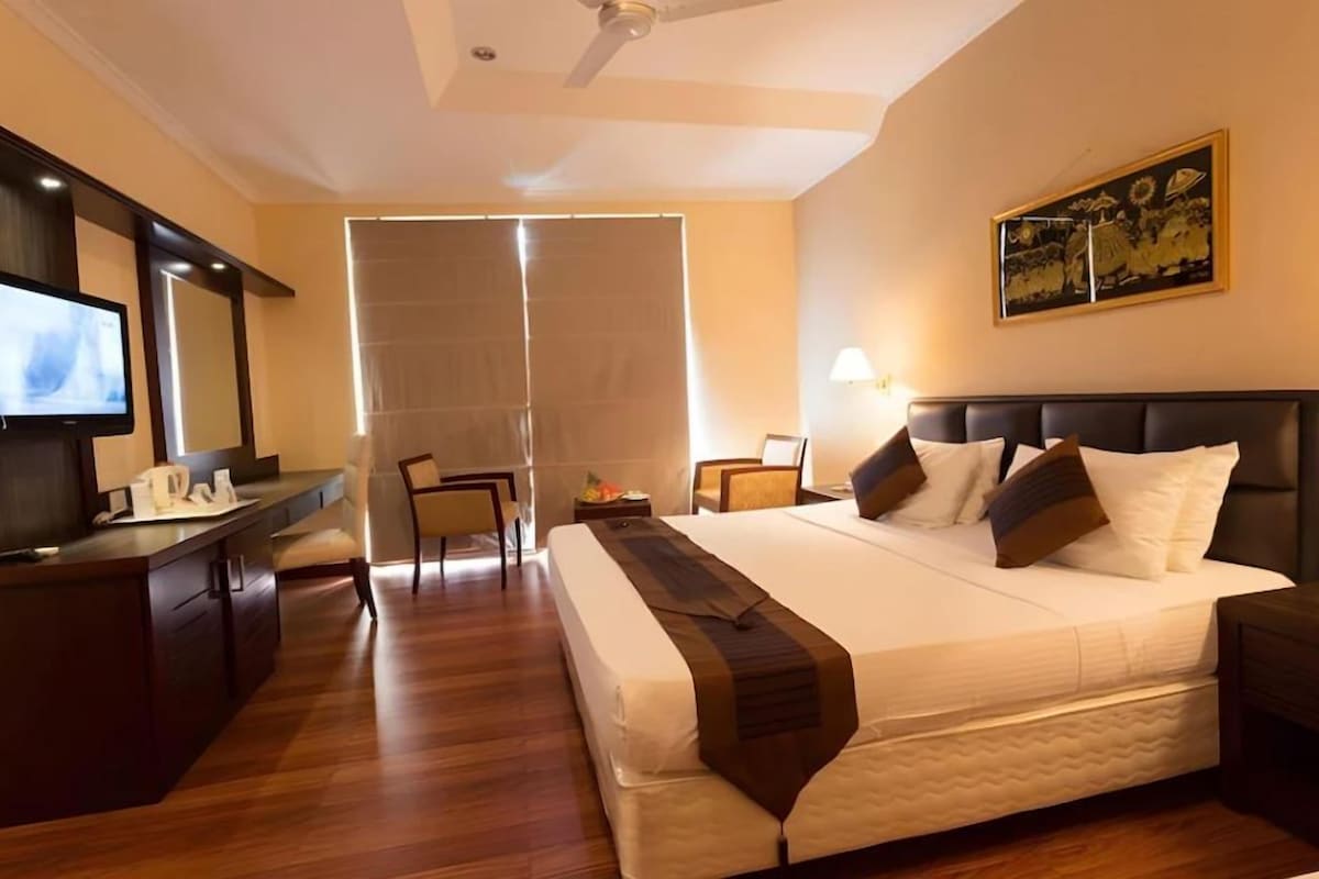 A hotel room with a bed, a desk, a chair, a television, and a painting on the wall.