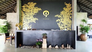 Mostrador de recepción con fondo negro y diseños florales dorados, una planta en maceta y un pequeño jardín de rocas.