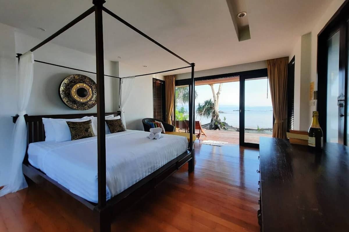 A four-poster bed with a view of the sea, a wooden floor, and a large decorative mirror.