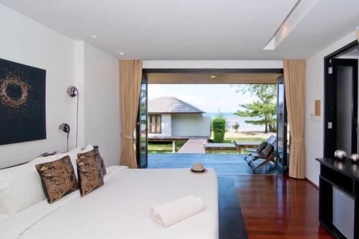 A modern hotel room with a large bed, a painting on the wall, and a view of the outdoor area.