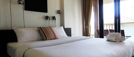 A neatly made bed with white linens, a striped pillow, and a rolled towel on the side.