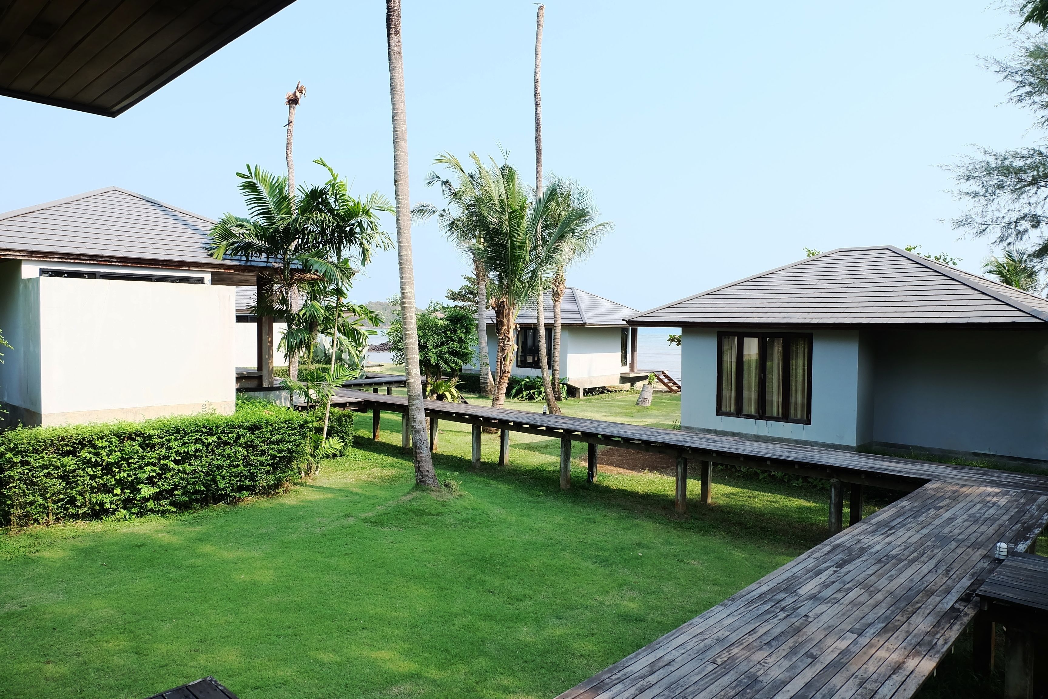 Un resort con varias edificaciones tipo bungalow, una terraza de madera y un césped bien cuidado.