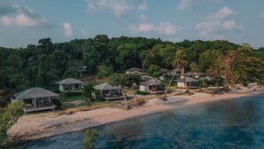 Un complejo turístico costero con villas frente a la playa, una playa arenosa y un bosque denso al fondo.
