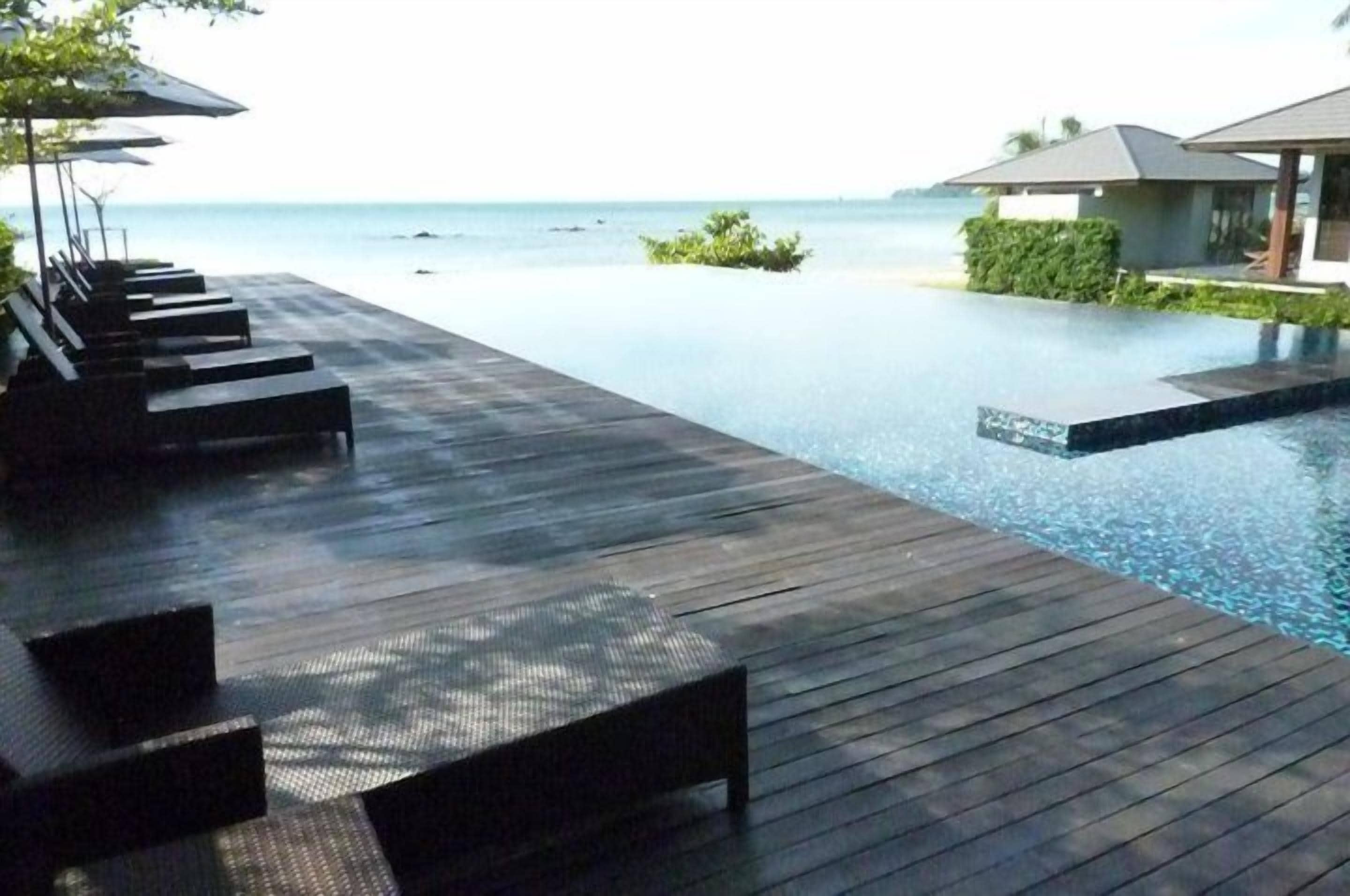 A wooden deck with lounge chairs and a pool extending to the ocean.
