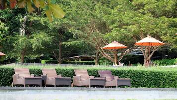 Une rangée de chaises longues sous des parasols orange, une haie bien entretenue et des arbres en arrière-plan.