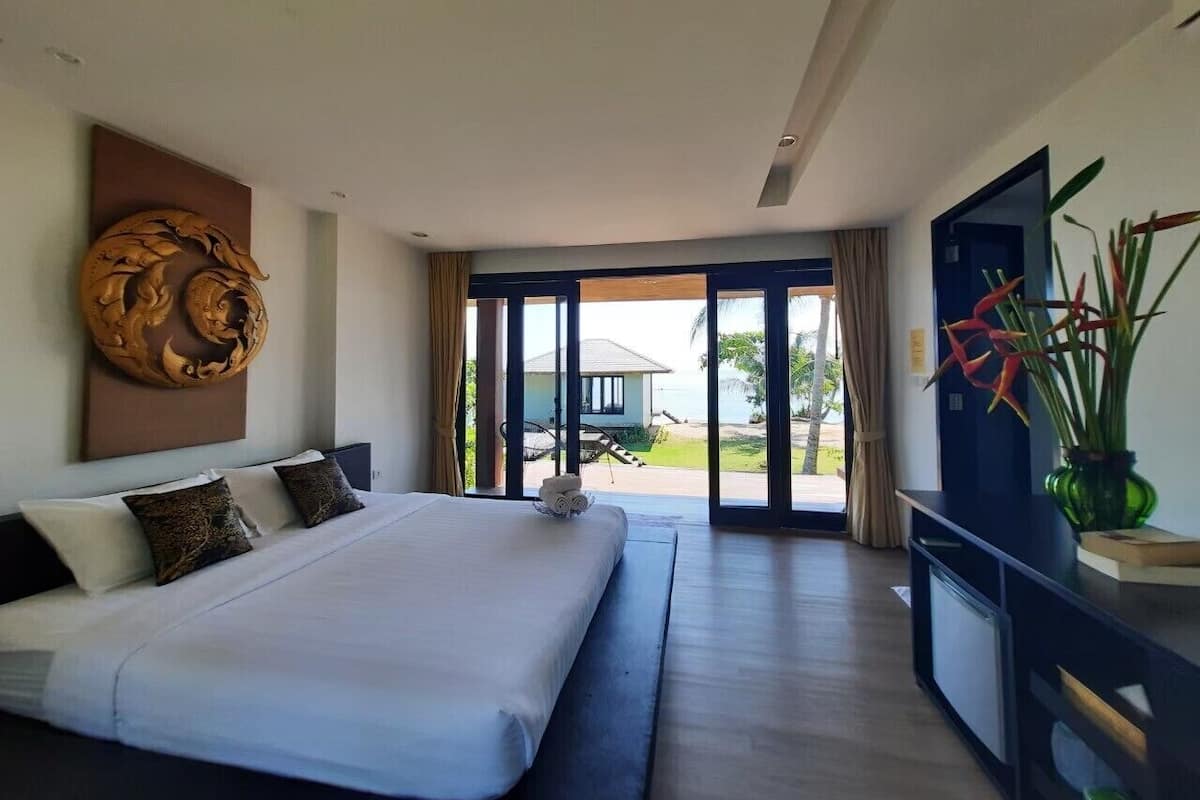 A bedroom with a large bed, a view of the outdoors, and a television on a stand.