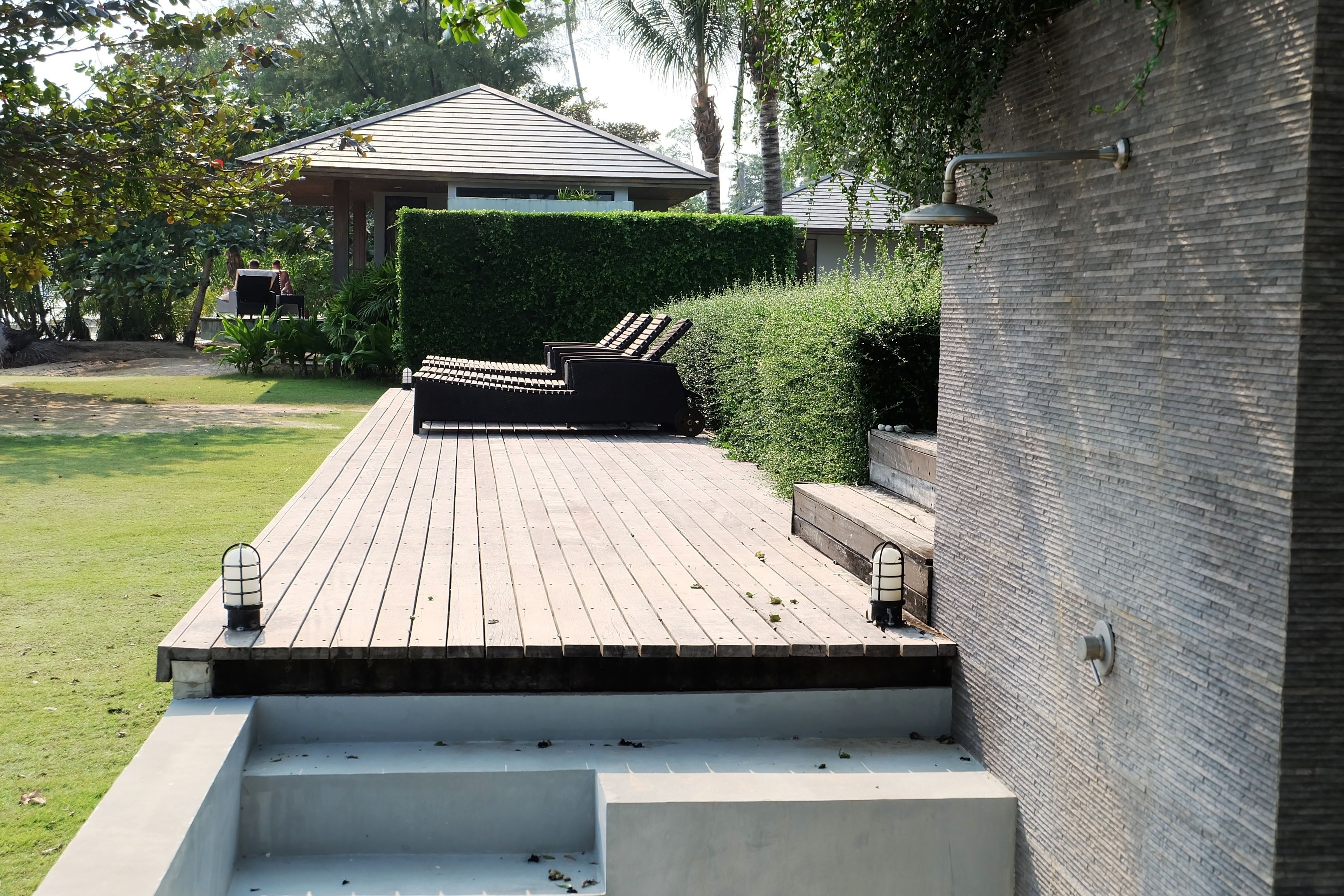 Una terraza de madera con escalones que llevan a una zona de estar, un muro de ladrillo y un edificio al fondo.