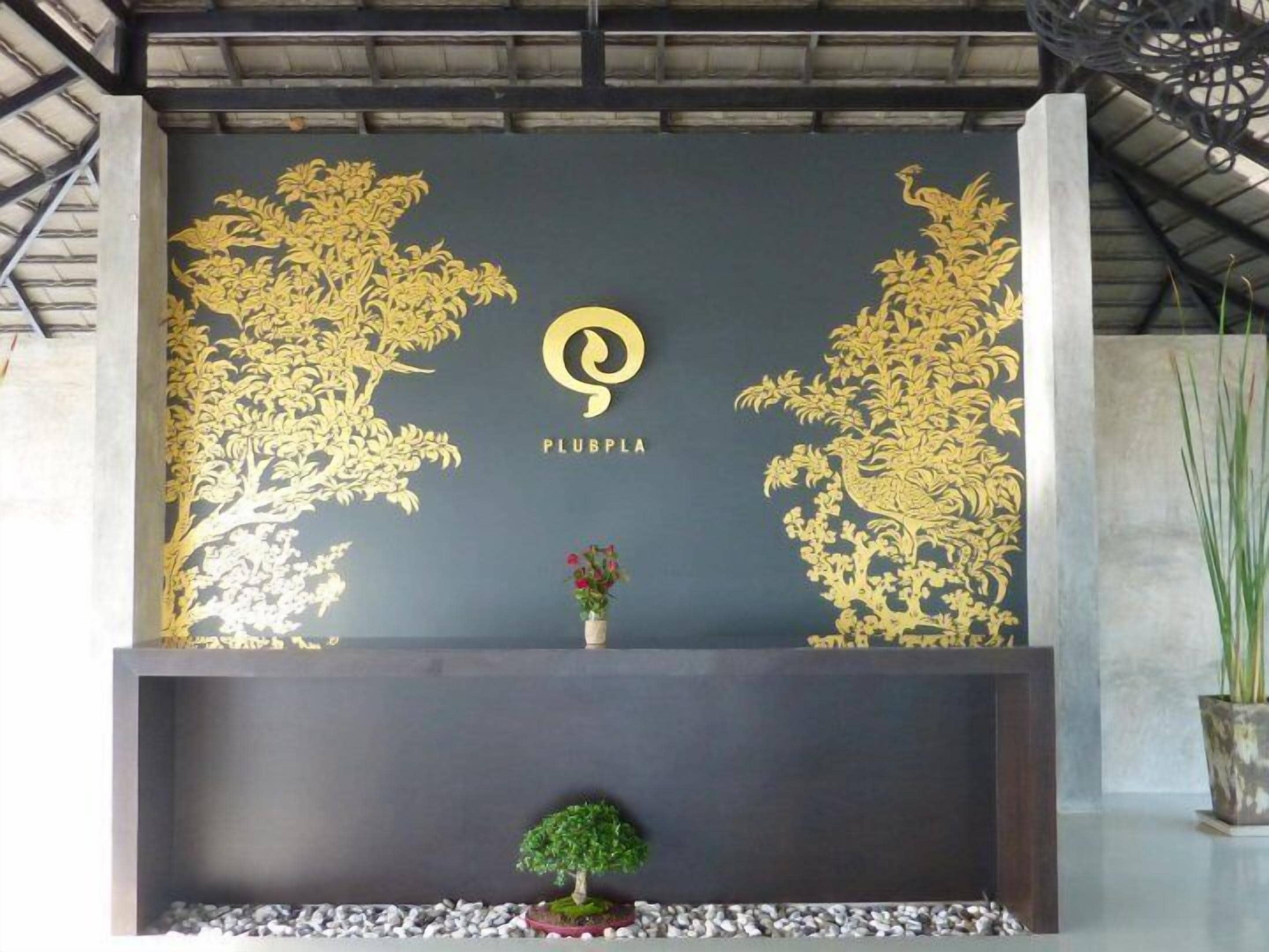 Een receptiegebied met een donkere wand met een goudkleurig bloemenpatroon en het logo 'PLUBPLA'.