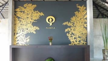 Een receptiegebied met een donkere wand met een goudkleurig bloemenpatroon en het logo 'PLUBPLA'.