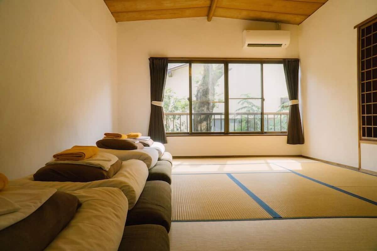 Ein Zimmer mit Tatami-Matten, niedriger Decke und einem großen Fenster mit Vorhängen.