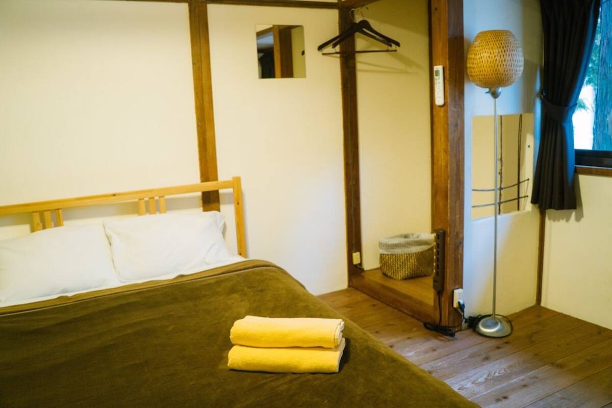 Ein Schlafzimmer mit einem Bett, einem Holz-Kopfteil, einer Hängelampe und einem kleinen Spiegel an der Wand.