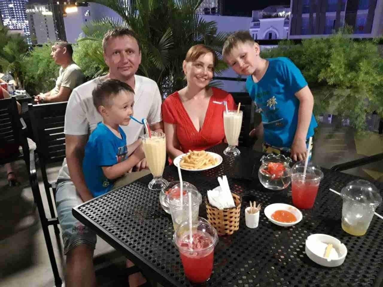 Eine Familie speist in einem Restaurant im Freien, ein Tisch für vier ist gedeckt, inklusive Getränke und einer Speise.