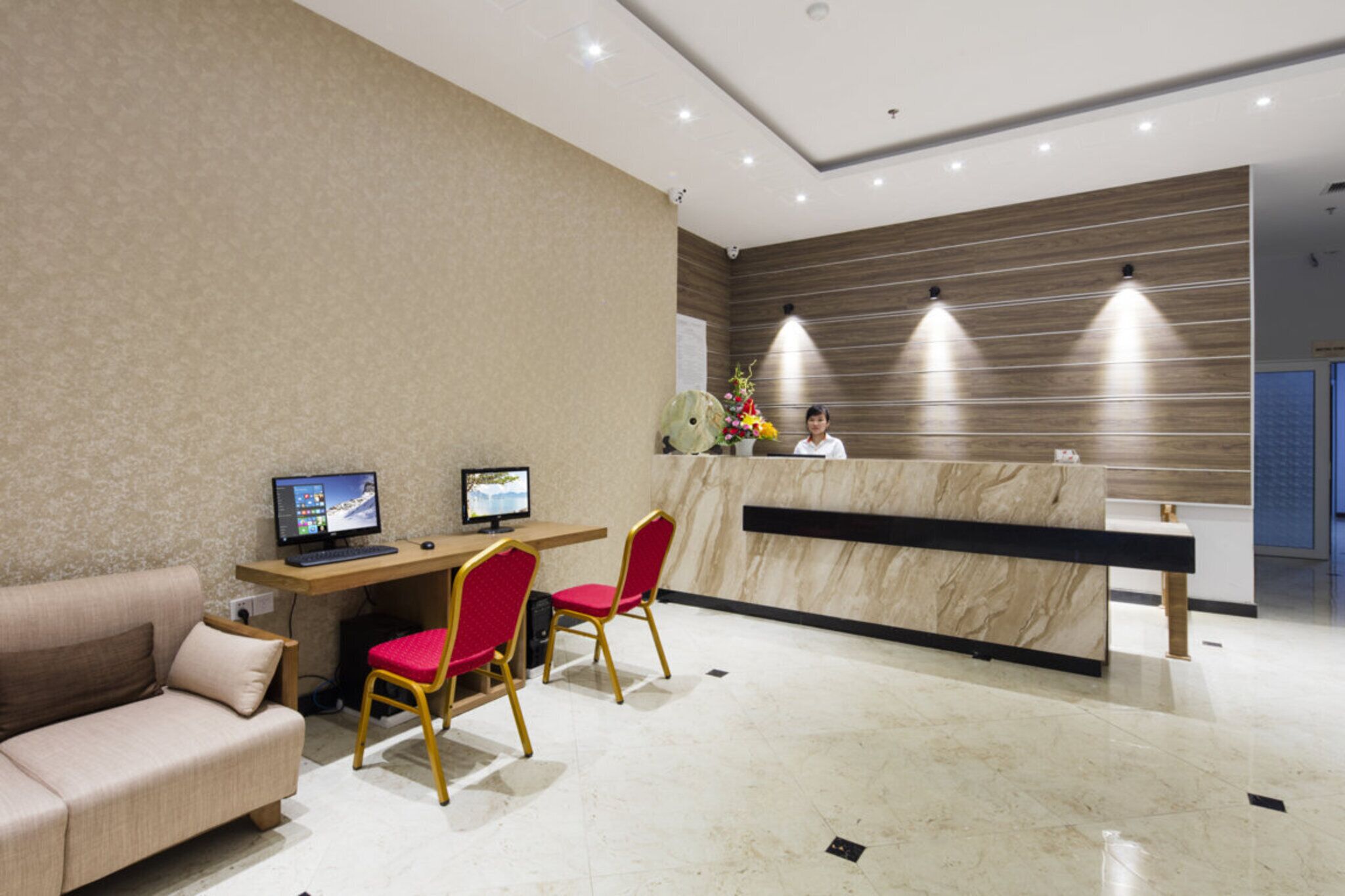 A reception area with a marble counter, two computers, a sofa, and red chairs.