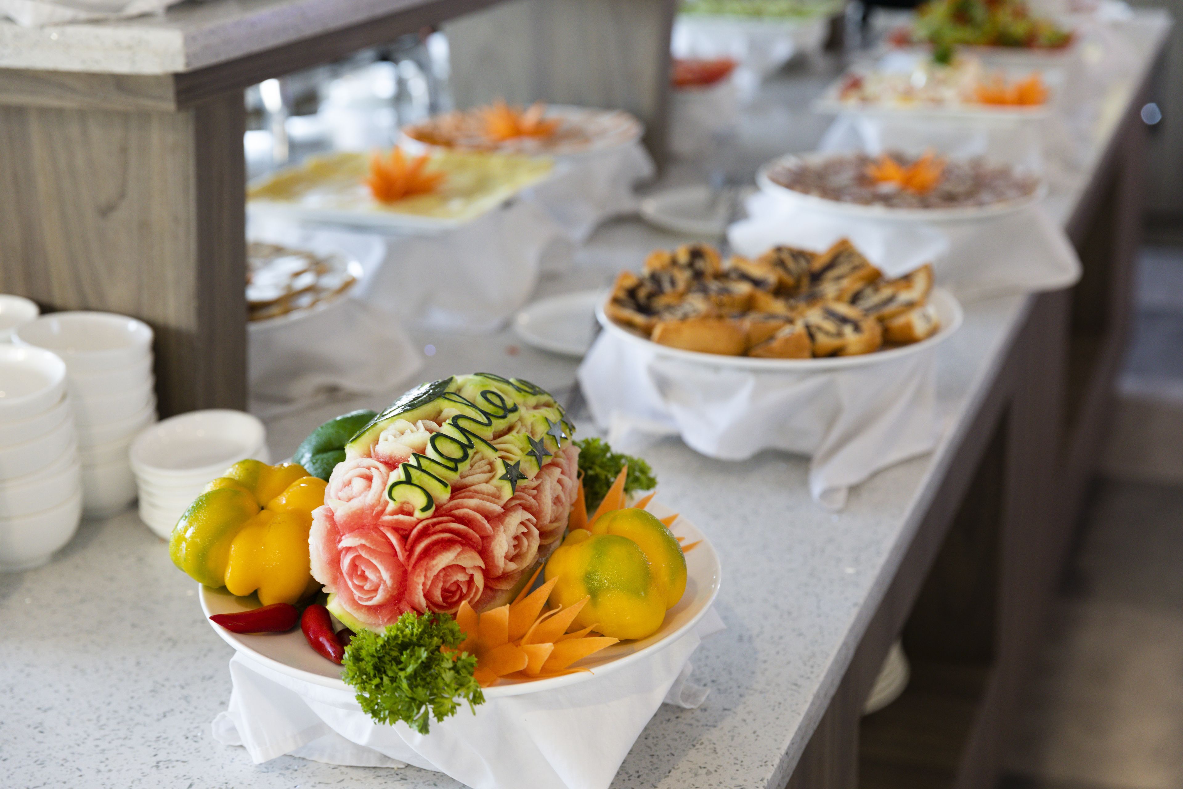 A buffet table with various dishes, including a centerpiece with a carved watermelon and vegetables.