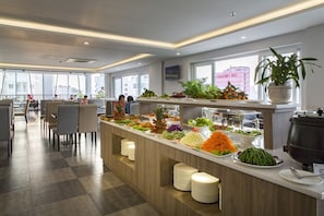 A buffet area with various food options, a seating area with chairs, and a large window with a view of a building.