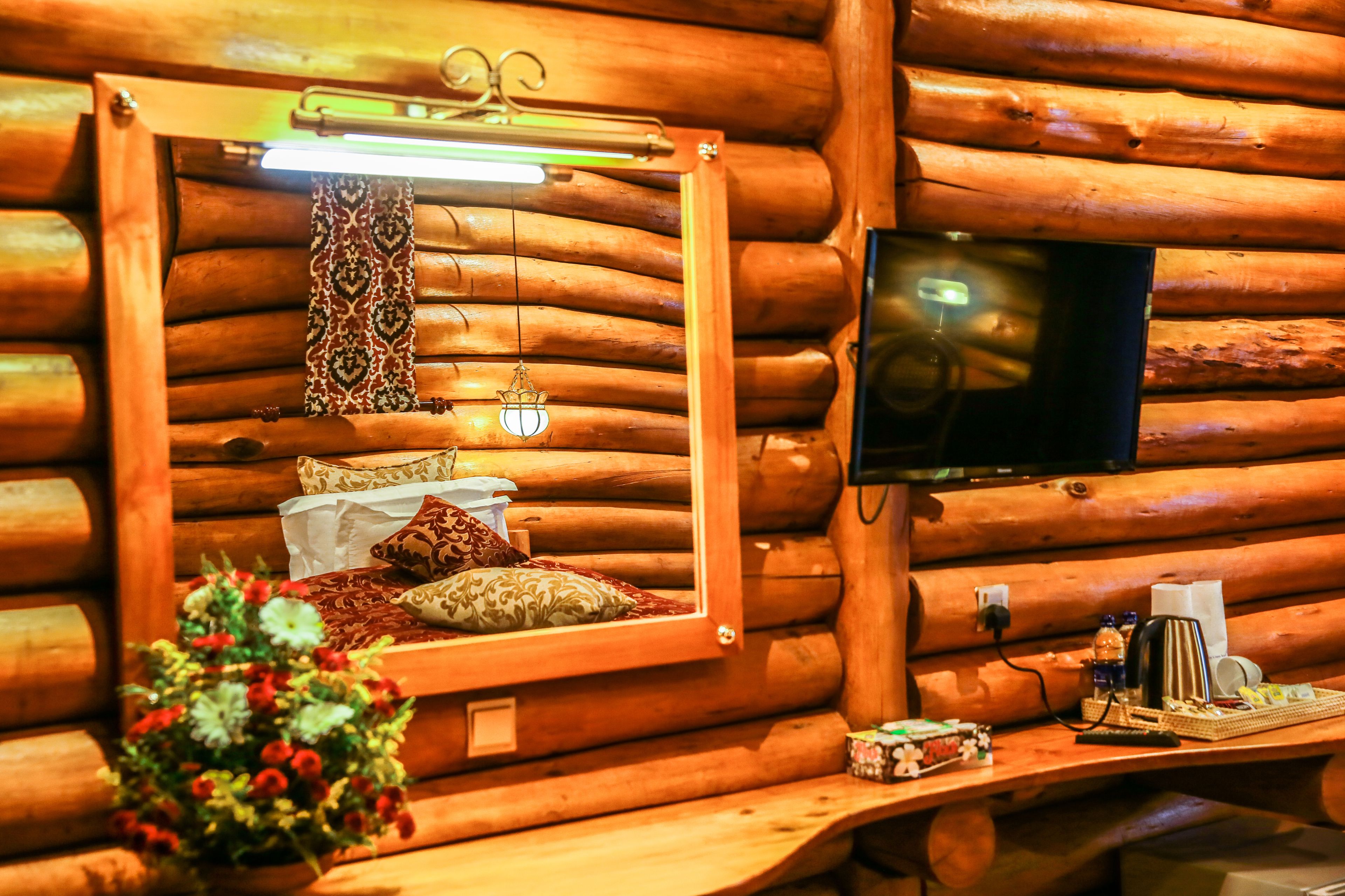 A cozy log cabin room with a wooden bed, a mirror, a television, and a small table with a coffee maker and snacks.