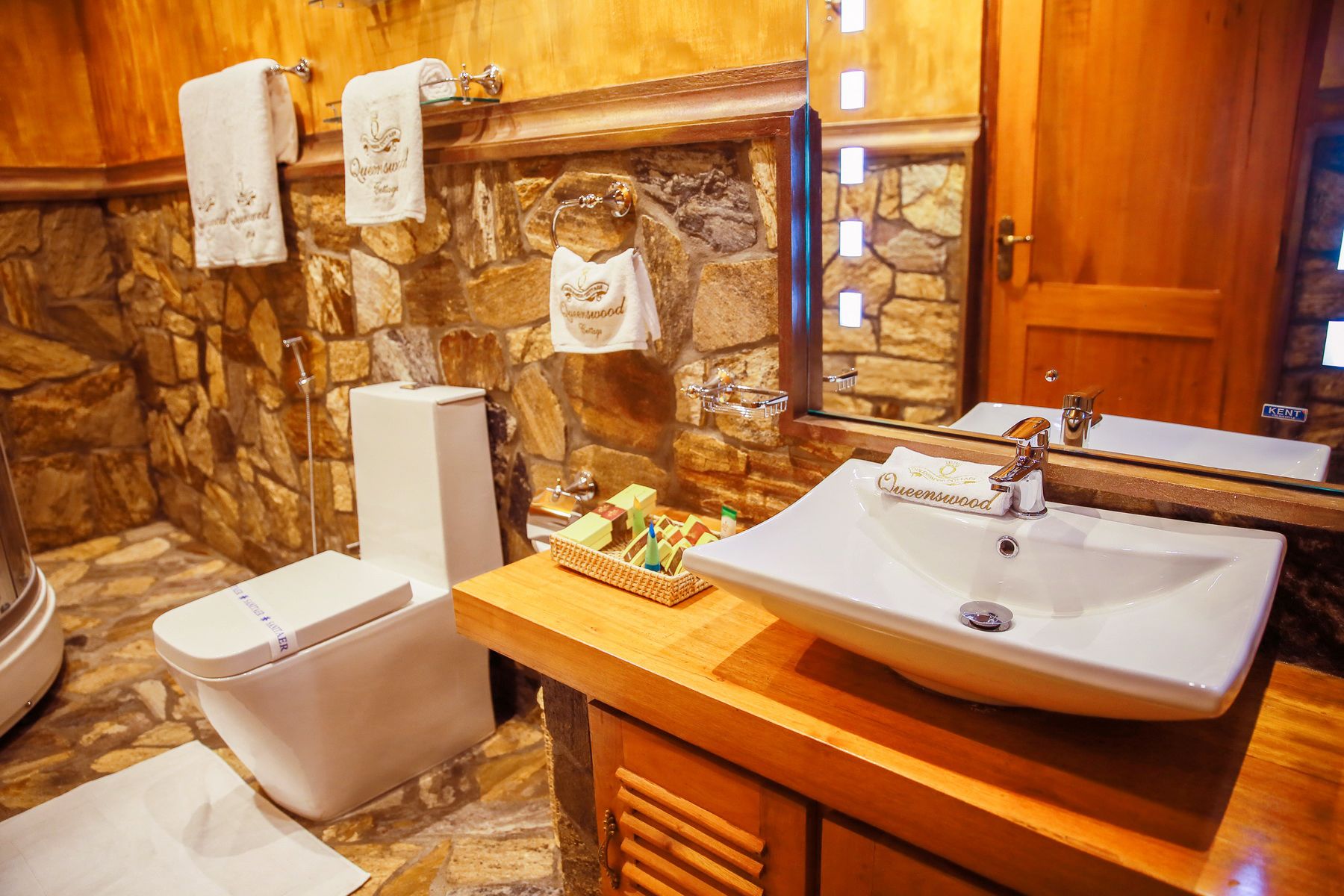 A bathroom with a stone wall, a white sink, a mirror, and a toilet.