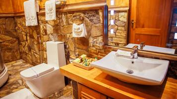 A bathroom with a stone wall, a white sink, a mirror, and a toilet.