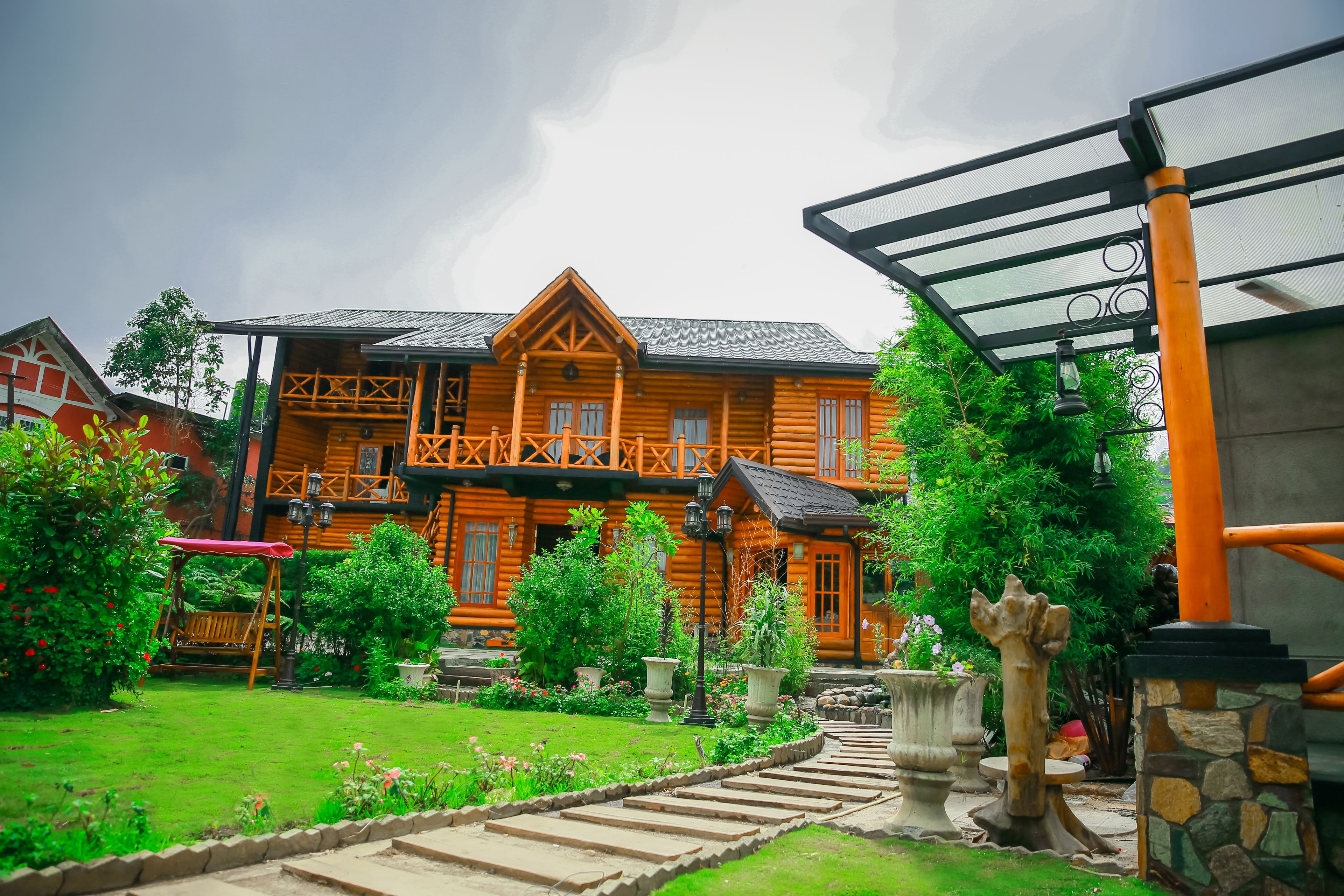 A wooden house with a porch, surrounded by a well-maintained garden and a stone pathway.