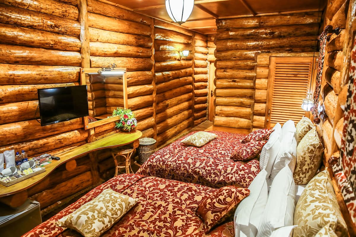 Una habitación tipo cabaña de madera con una cama, un escritorio, un televisor y una ventana con contraventanas.