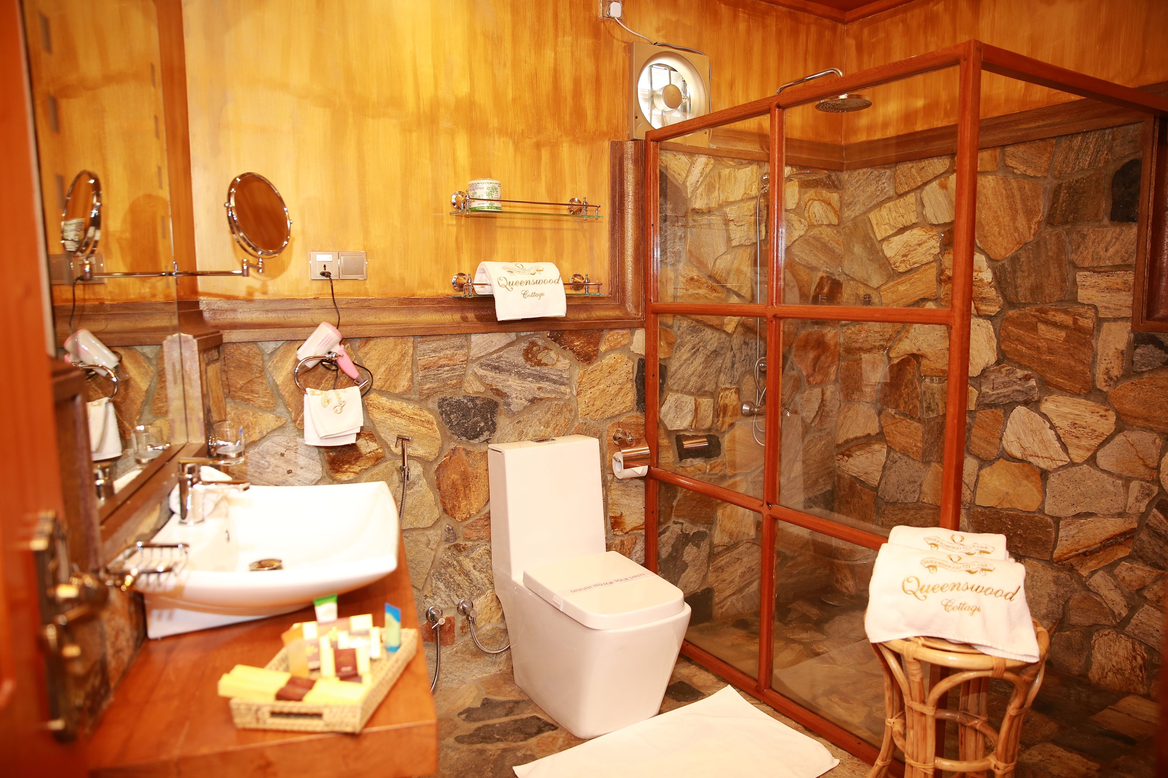A bathroom with a stone wall, a white sink, a toilet, and a glass-enclosed shower.
